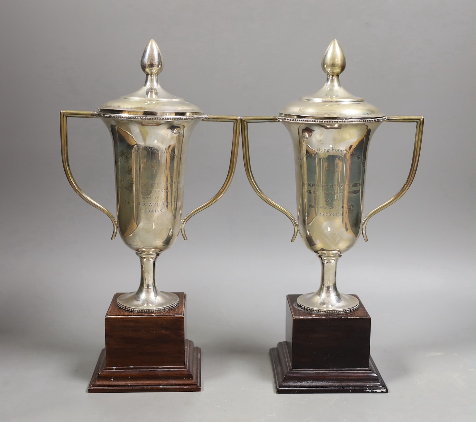 A pair of Royal Hong Kong Jockey Club sterling presentation two handled trophy cups and covers, fixed to wooden plinth bases, height of cups 26cm.